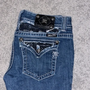 Blå jeans med detaljer från Miss Me - Snygga blå jeans från Miss Me med unika detaljer. Byxorna har diamanter på bakfickorna och alla diamanter är kvar