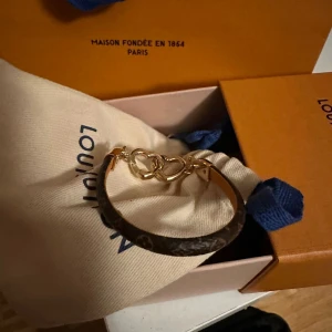 Armband från Louis Vuitton med hjärtdetalj - Elegant armband från Louis Vuitton med en stilren design i brunt och guld. Armbandet har en vacker hjärtdetalj i guld som ger en lyxig touch. Perfekt accessoar för att lyfta vilken outfit som helst.                                                                    Köptes från Louis Vuitton i Stockholm för 3850 kr den 1/8-24 Kvitto medföljer  Original förpackning och påse medföljer Aldrig använd