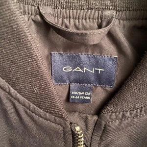 Mörkblå bomberjacka från GANT - Säljer nu en snygg mörkblå bomberjacka från GANT i storlek 13-14 år men sitter lite större. Personen på bilden är 177 cm lång och väger 65 kg. Nypris ca 1500 kr. Nästan aldrig använd. Hör av dig för frågor!