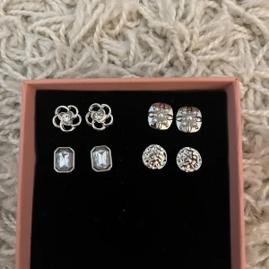 Set med fyra par silverörhängen. - Säljer ett set med fyra par silverörhängen. Inkluderar blommiga, fyrkantiga och runda designer med glittriga detaljer. Perfekt för att mixa och matcha till olika tillfällen. Säljer alla för 200kr.
