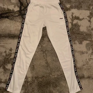 Fila byxor - Snygga vita träningsbyxor från Fila med elastisk midja och logotyp längs sidorna. Perfekta för sport och fritid samt stilig och skön för sommaren. Byxorna har knappt använts och och i nytt skick