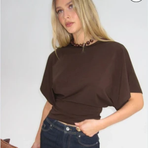 Brun topp med korta ärmar - Snygg brun topp med korta ärmar och en tight passform i midjan. Perfekt för en stilren look.