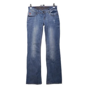 Blå bootcut jeans med broderad ficka - Snygga blå bootcut jeans med en unik broderad detalj på bakfickan. De har en klassisk femficksdesign och en lågmidjad passform. Bootcut och såååå snygga!🩷