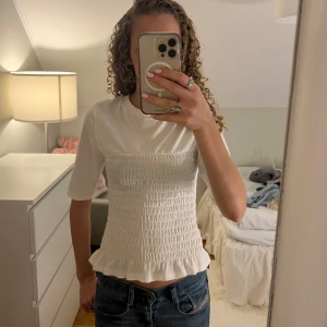 Vit topp med smock från HM - Säljer denna söta vita toppen med smockdetaljer och volangkant💕🥹 Toppen har trekvartsärm och en rund halsringning. Passar både till skolan eller fester🥰Priset kan diskuteras vid snabb affär! Den är i storlek Xxs men passar även xs och kanske s då den är väldigt stretchig.