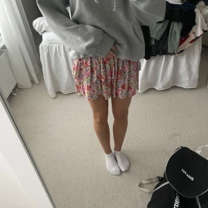 Blommig kortkjol - Söt blommig kortkjol från Vila i rosa, rött och grönt med volangdetaljer. Perfekt för en somrig look.