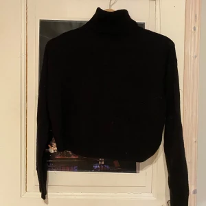 Svart stickad polotröja - Säljer en svart stickad polotröja med lång ärm. Tröjan är croppad och har en hög krage som ger en stilren look. Perfekt för kyligare dagar.