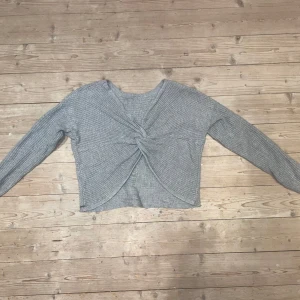 Grå stickad tröja från Hollister - Säljer en snygg grå stickad tröja från Hollister med en unik twistdetalj framtill. Tröjan har långa ärmar och en croppad passform.