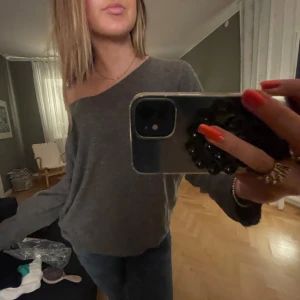 Grå oneshoulder tröja - Säljer en väldigt fin grå tröja med bred halsringning och lång ärm. Tröjan har en lös passform och är tillverkad i ett mjukt material💝💝Den har ingen angiven storlek men passar mig som brukar ha S💕