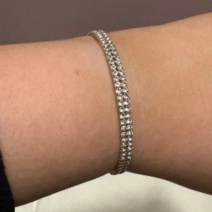 Glittrigt armband i silver - Snyggt och elegant armband i silver med glittrande stenar. Perfekt för att ge en touch av glamour till din outfit. Armbandet är smalt och stilrent, vilket gör det lätt att matcha med andra smycken.