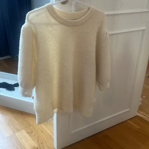 Vit tröja från Gina Tricot - Mysig vit tröja från Gina Tricot med rund halsringning och trekvartsärmar. Perfekt för kyliga dagar när du vill ha något bekvämt och stilrent. Tröjan har en mjuk och fluffig textur som ger en extra mysfaktor.