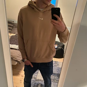 Beige hoodie från Nike - Säljer en snygg beige hoodie från Nike med klassisk logga på bröstet. Har tagit bort snörena då de va för långa och inte så snygga, men förutom det finns det inga skador på tröjan. Nypris: 1200kr