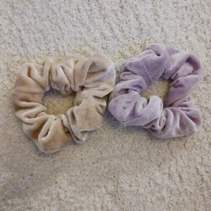 Två scrunchies i sammet - Två mjuka scrunchies i sammet, en i beige och en i lila. Perfekta för att ge en stilfull touch till din frisyr.