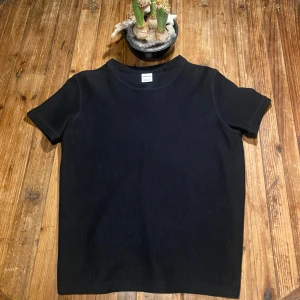 Svart stickad t-shirt från Bershka - Snygg svart stickad t-shirt från Bershka i ett texturerat material. Den har en klassisk rund hals och korta ärmar, perfekt för en stilren look.