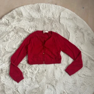 Röd kofta från Holly & Whyte - Säljer en snygg röd kofta från Holly & Whyte by Lindex. Koftan har långa ärmar och knappar framtill. Perfekt för att lägga till en färgklick i din garderob!