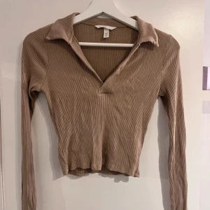 Topp - Långärmad ribbad topp ifrån H&M, med v-ringning och en liten krage, färgen skulle jag säga är en blandning mellan brun och beige. toppen är använd men i bra skick