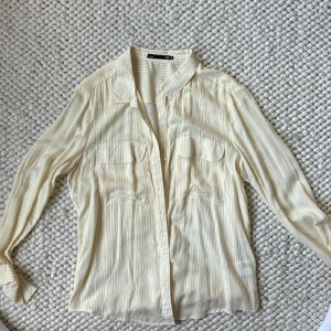 Gul- och vitrandig skjorta från Etay - Säljer en superfin gul- och vitrandig skjorta från lager157. Den har långa ärmar och knappar framtill. Skjortan är i storlek M och är perfekt för vår och sommar. Den har två bröstfickor som ger en snygg detalj. Materialet känns lätt 