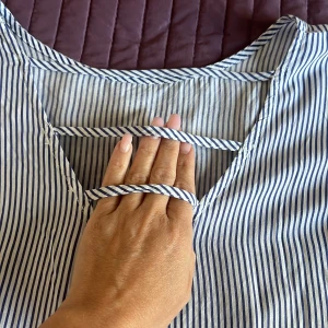 Randig blus från LC Waikiki - Säljer en snygg randig blus från LC Waikiki i storlek L. Den har en avslappnad passform med trekvartsärmar och ett stilrent randigt mönster i blått och vitt. Blusen har en fin detalj med korsade band i ryggen. Perfekt för både vardag och lite mer uppklädda tillfällen!