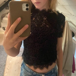 Svart spetsblus - Säljer en superfin svart spetsblus med korta ärmar. Den är croppad och har ett vackert mönster i spetsen. Perfekt för en festlig kväll eller en utekväll med vänner. Blusen är i bra skick och redo för nya äventyr! Jag har ett linne under!