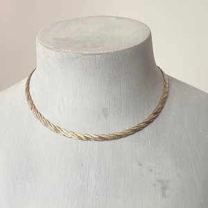 Elegant guldhalsband i flätad design - Säljer ett stilrent och elegant halsband  med en vacker flätad design. Halsbandet är i nyskick och har en säker låsmekanism. Perfekt för både vardag och festliga tillfällen. Det är märkt med 925, vilket indikerar att det är av hög kvalitet.