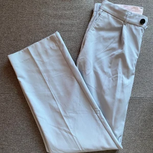 Weekday Conrad Wide Trousers - strl. 46 - Säljer ett par stilrena ljusblå byxor från Weekday helt nya. De har en klassisk design med knappar och bälteshällor. Perfekta för både vardag och fest! 