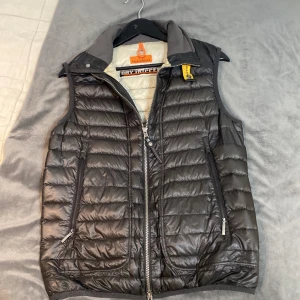Svart dunväst från Parajumpers - Säljer en snygg svart dunväst från Parajumpers. Den har en dragkedja framtill och praktiska fickor. Perfekt för höst och vår när du vill hålla dig varm men ändå se stilren ut. Västen är i nyskick och har en normal passform. Inuti är den ljus med flera fickor för extra förvaring. Väldigt sliten innuti, och många tidigare, men lagade hål, så västen är inte så tjock,pågrund av dunförlust, därav priset. Riktigt bra köp för en stilren väst!
