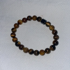 Armband med tigeröga pärlor - Snyggt armband med runda tigeröga pärlor i bruna och gyllene nyanser. Perfekt för att ge en naturlig touch till din stil. Elastiskt band för enkel passform. Passar både till vardags och festliga tillfällen.