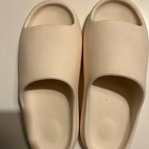 Beige sandaler - Säljer ett par stilrena och bekväma beige sandaler. Perfekta för sommaren med sin enkla design och mjuka material. De har en bred rem över foten och en räfflad sula för extra grepp. Passar perfekt för en avslappnad dag på stranden eller hemma.
