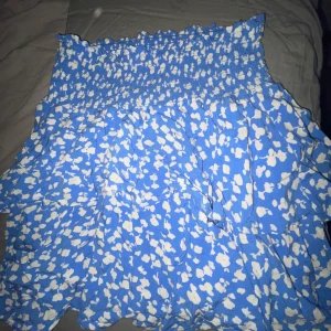 Blå och vit blommig kjol från Salsa - Säljer en superfin blå kjol med vita blommor från Ullared. Kjolen har en elastisk midja som ger en bekväm passform och volanger som ger en söt look. Perfekt för sommardagar eller en avslappnad vårutflykt!