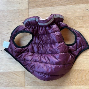 Vinröd hundjacka med dragkedja - superfin lila quiltad hundjacka i storlek 25 cm. Den är gjord av 100% polyester och har en praktisk dragkedja framtill. Perfekt för kyliga höst- och vinterpromenader. Jackan har en reflekterande rand på kragen för extra säkerhet i mörkret. 🐾använd av min hund som valp endast 2-3 gånger