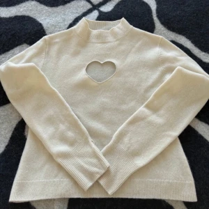 Vit  tröja med hjärtformad detalj från Cloeys - Säljer en stilren vit tröja från Cloeys med en unik hjärtformad detalj framtill. Tröjan har långa ärmar och en ribbad kant vid halsen och ärmsluten. Populär och även slutsåld tröja i 100% merinoull 