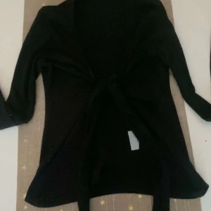 Svart kofta med knytband - Elegant svart kofta med knytband framtill. Perfekt för lager-på-lager och ger en stilren look. Långärmad design som passar bra till både vardag och mer uppklädda tillfällen.