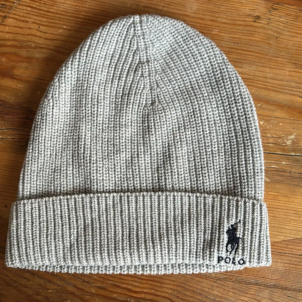 Snygg grå ribbad mössa från Polo Ralph Lauren med broderad logga framtill. Perfekt för kyliga dagar och ger en stilren look. Tillverkad i mjukt material för extra komfort.. Asusteet.