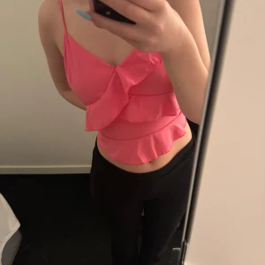 Rosa volangtopp - Snygg rosa topp med volangdetaljer och smala axelband. Perfekt för en somrig look eller en utekväll. Toppen har en feminin och lekfull design.