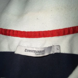 Randig pikétröja från Dressmann - Säljer en stilren randig pikétröja från Dressmann i svart och vitt. Tröjan har korta ärmar och en klassisk krage med knappar. Perfekt för en avslappnad look.