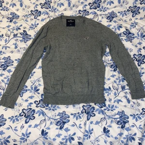 Grå tröja från Hollister - Säljer en stilren grå tröja från Hollister i storlek XS. Tröjan har en diskret logga på bröstet och är tillverkad i ett mjukt material med ribbade muddar vid ärmslut och nederkant. Perfekt för en avslappnad look. Obs! Några  fläckar 