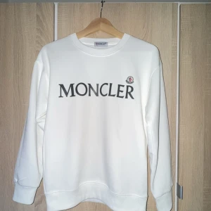 Vit sweatshirt från Moncler - Säljer en stilren vit sweatshirt från Moncler med deras ikoniska logga tryckt på framsidan. Tröjan har långa ärmar och en klassisk rund halsringning. Perfekt för en avslappnad och trendig look.