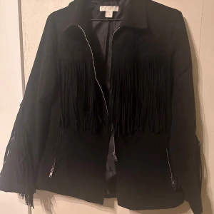 Svart jacka med fransar från H&M - Snygg svart jacka från H&M med fransar på fram- och baksidan. 
