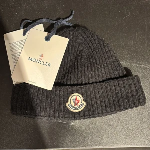Moncler mössa - Snygg svart ribbad mössa från Moncler med broderad logotyp framtill. Perfekt för kyliga dagar och en stilren look.