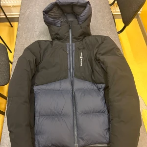 Sail Racing svart och blå dunjacka - Säljer en svart och blå dunjacka från Sail Racing. Jackan har en huva och dragkedja framtill. Den är perfekt för kalla dagar med sin 600 fill power och sitter väldigt bekvämt. Pris kan diskuteras för ett snabbköp.