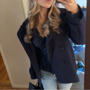 Mörkblå kappa - Snygg mörkblå kappa med dubbelknäppning ifrån design by si. Perfekt för våren och vintern, ger en stilren look. Passar bra till både jeans och mer uppklädda outfits. Kappan är i nyskick och säljs för ett bra pris. Hör av er vid frågor!💕💕