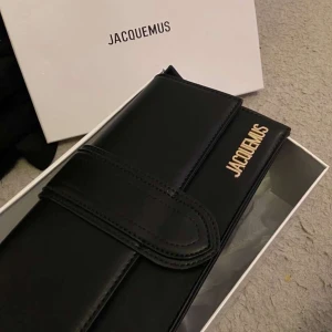Svart axelväska från Jacquemus - Elegant svart axelväska från Jacquemus i skinn med guldfärgade detaljer. Väskan har en stilren design med en justerbar axelrem och en praktisk stängning. Perfekt för att ge en lyxig touch till din outfit. Pris kan diskuteras