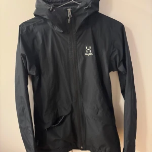 Svart vindjacka från Haglöfs - Snygg och funktionell svart vindjacka från Haglöfs i dam modell. Perfekt för blåsiga dagar och utomhusaktiviteter. Jackan har en stilren design med Haglöfs-logga på bröstet.