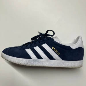 Adidas Gazelle i mörkblå mocka - Snygga Adidas Gazelle sneakers i mörkblå mocka med vita detaljer och snörning. Den klassiska designen har de ikoniska tre ränderna på sidan och en vit sula. Använda endast 5ggr.
