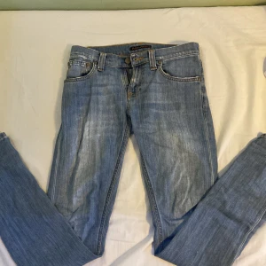 Blå jeansbyxor från Nudie - Snygga blå jeansbyxor från Nudie med klassisk femficksdesign och knappgylf. Perfekta för en avslappnad stil. Jeansen är slim fit och är tillverkade i slitstarkt denim. Storleken är W26 L32