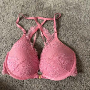 Rosa spets-BH från Hunkemöller - Säljer en söt rosa BH från Hunkemöller med spetsdetaljer och justerbara axelband. Den har en elegant design med en liten guldfärgad detalj framtill. Den är oanvänd!!