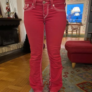 Röda jeans med vita sömmar - Snygga röda jeans från True Religion med kontrasterande vita sömmar. Byxorna har en bootcut-stil och är lågmidjade med klassiska femficksdetaljer. Perfekta för att ge en färgklick till din outfit!