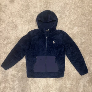 Mörkblå fleecejacka från Polo Ralph Lauren - Säljer en mysig mörkblå fleecejacka från Polo Ralph Lauren med huva och dragkedja. Nypris ~ 2500kr, mitt pris 1099kr. Jackan har två fickor framtill och ett broderat logotypmärke på bröstet. Perfekt för kyliga dagar och vid avslappnade tillfällen! Storlek S. 