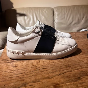 Valentino Open Garavani sneakers - Säljer ett par snygga Valentino Garavani sneakers i vitt och blått. De är i väldigt bra skick med lite slitage på sulorna. Perfekta för både vardag och fest! Säljer för 2399 kr. Nypris ligger runt 6000 kr