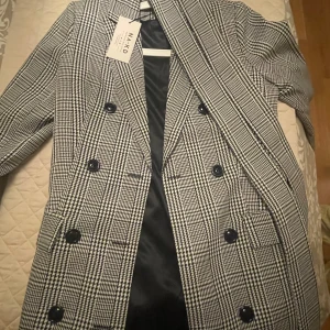 Rutig kappa - Snygg rutig kappa från NA-KD i svart och vit. Har aldrig använts och prislappen står kvar. Har inget kvitto då det var en gåva ☺️