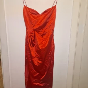 Röd klänning  - Snygg röd klänning med smala axelband och v-ringad urringning. Tillverkad i ett glansigt material som ger en elegant look. Perfekt för festliga tillfällen. Garderobsrensning så kika gärna på övriga auktioner.